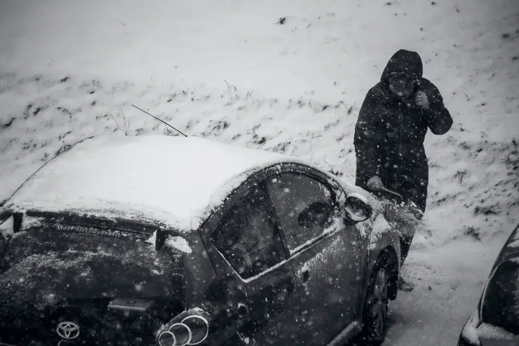 Hombre con su coche km 0 cubierto de nieve